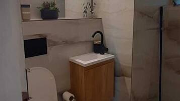 A modern bathroom with a toilet, sink, mirror, and a shower area.