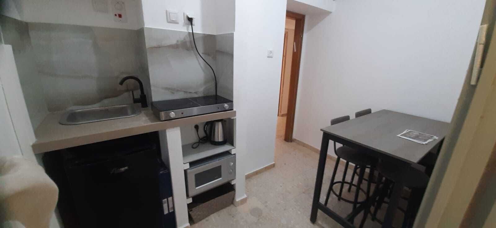 A compact kitchen with a sink, stove, microwave, and a small dining table with stools.