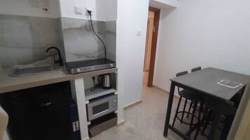 A compact kitchen with a sink, stove, microwave, and a small dining table with stools.