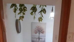 A hallway leading to a dining area with a table and chairs, a painting on the wall, and hanging plants. - 1-bedroom, AC, Wifi, 10 minutes from Rashbi, 3 minutes from Safed Old City (Safed)