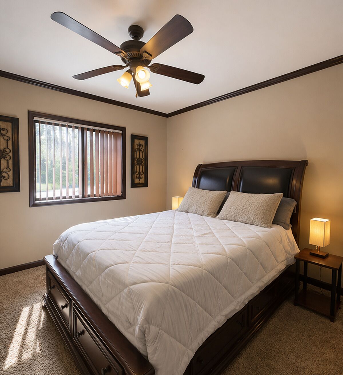 A bedroom with a bed, a ceiling fan, a window with blinds, and a nightstand with a lamp.