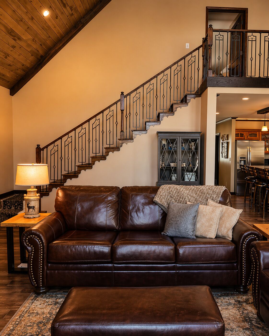 A spacious living room with a leather couch, a wooden staircase, and a kitchen area in the background.