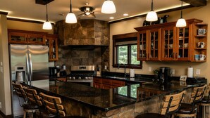 Cocina con una isla de piedra, taburetes de bar, armarios de madera, electrodomésticos de acero inoxidable e iluminación colgante.