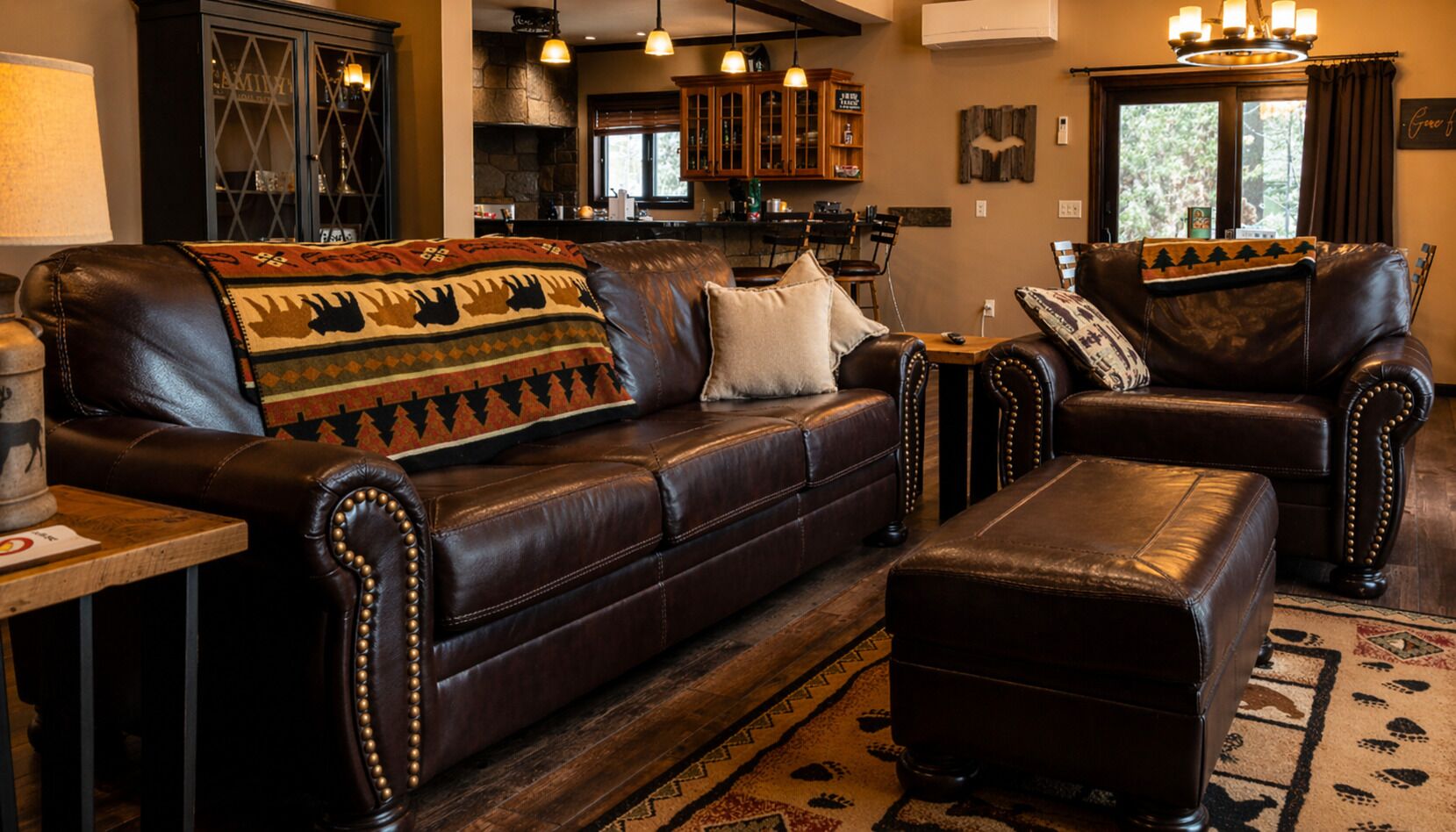 A leather sofa with a patterned throw blanket, a matching ottoman, and a wooden coffee table with a lamp.