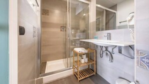 A modern bathroom with a glass-enclosed shower, a wooden shelf with toiletries, and a white sink. - Cosy studio located in heart of Born (Barcelona)