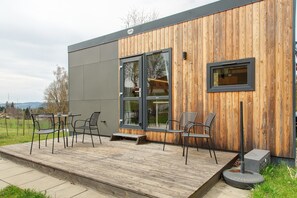 Ein modernes Gebäude mit Holzfassade, einer Terrasse mit Sitzgelegenheiten und einem großen Fenster.