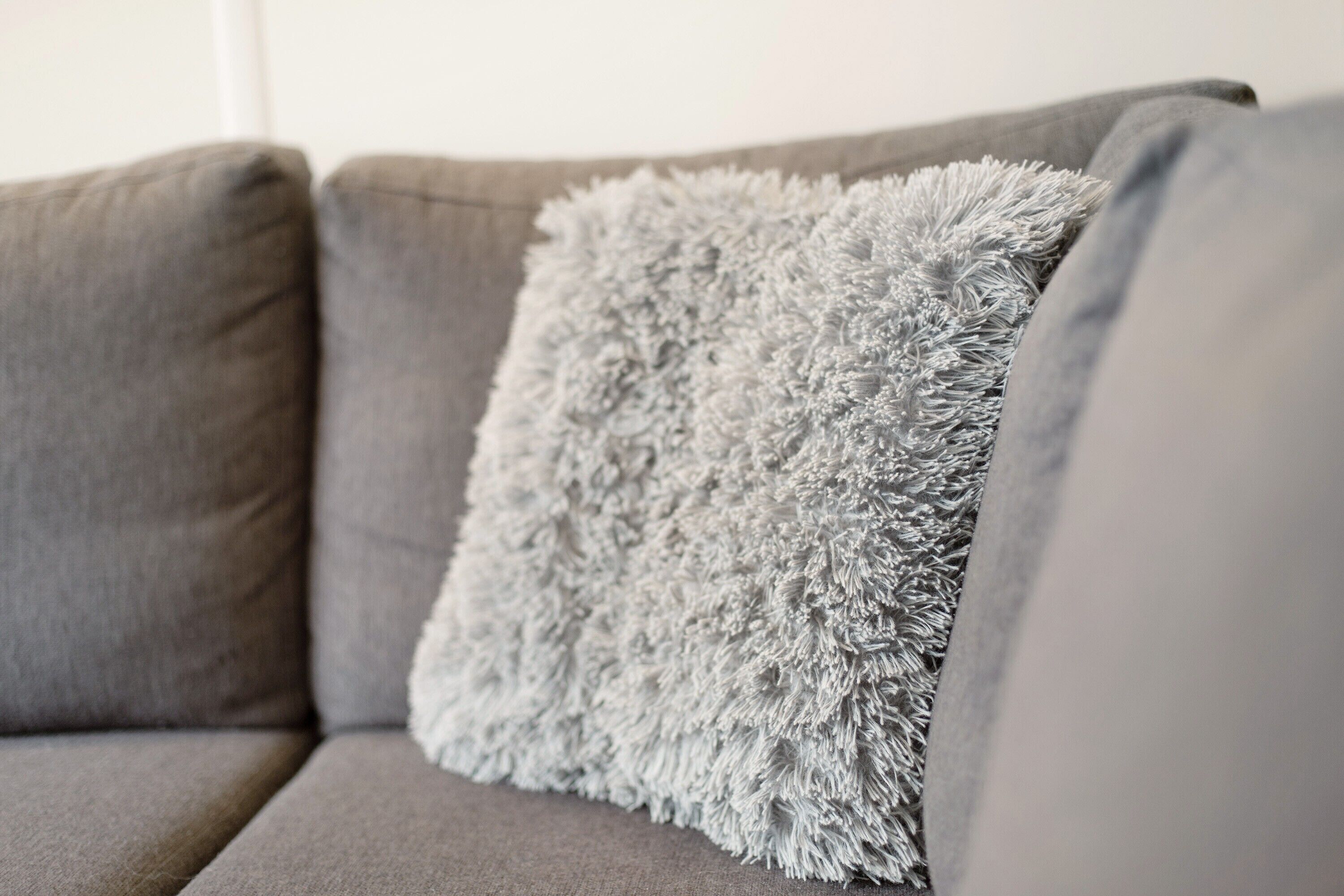 A grey sofa with a fluffy grey pillow.