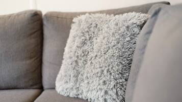 A grey sofa with a fluffy grey pillow.