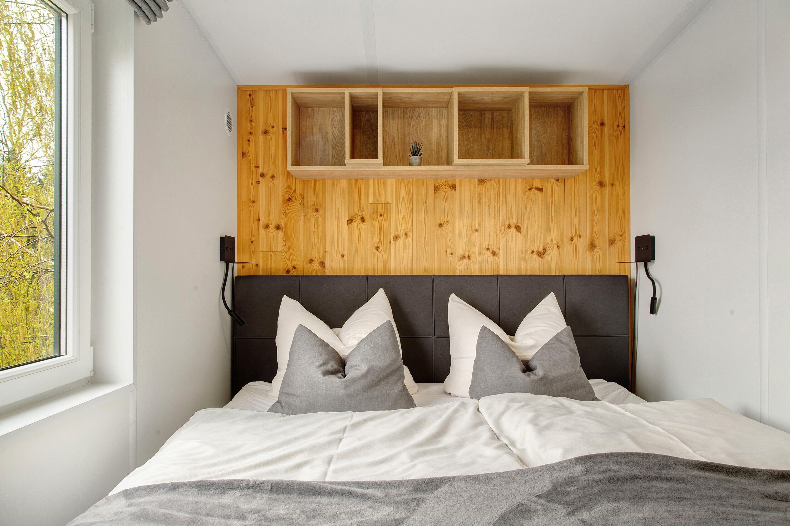 Ein Schlafzimmer mit einem Bett, einem Fenster, einem Holzkopfteil und einem Regal über dem Bett.
