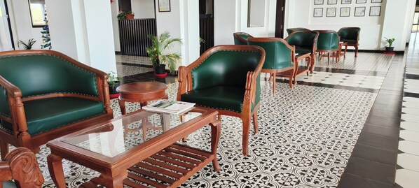 A lobby with green upholstered chairs, a wooden coffee table, and patterned floor tiles.