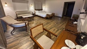 A hotel room with a wooden floor, two single beds, a sofa, a chair, and a small dining table with plates and cups. - Royal gold feildd club resorts (Dapoli)
