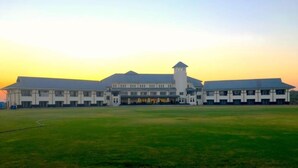 A large building with a central tower, multiple wings, and a spacious lawn in front. - Royal gold feildd club resorts (Dapoli)