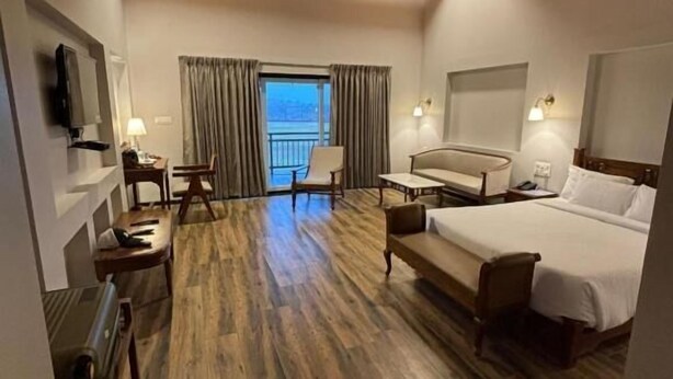 A hotel room with a wooden ceiling, a bed, a desk, a chair, and a view of the outdoors. - Royal gold feildd club resorts (Dapoli)