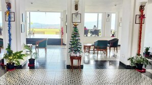 A hotel lobby with a tiled floor, seating areas, potted plants, and a view of the outdoors. - Royal gold feildd club resorts (Dapoli)
