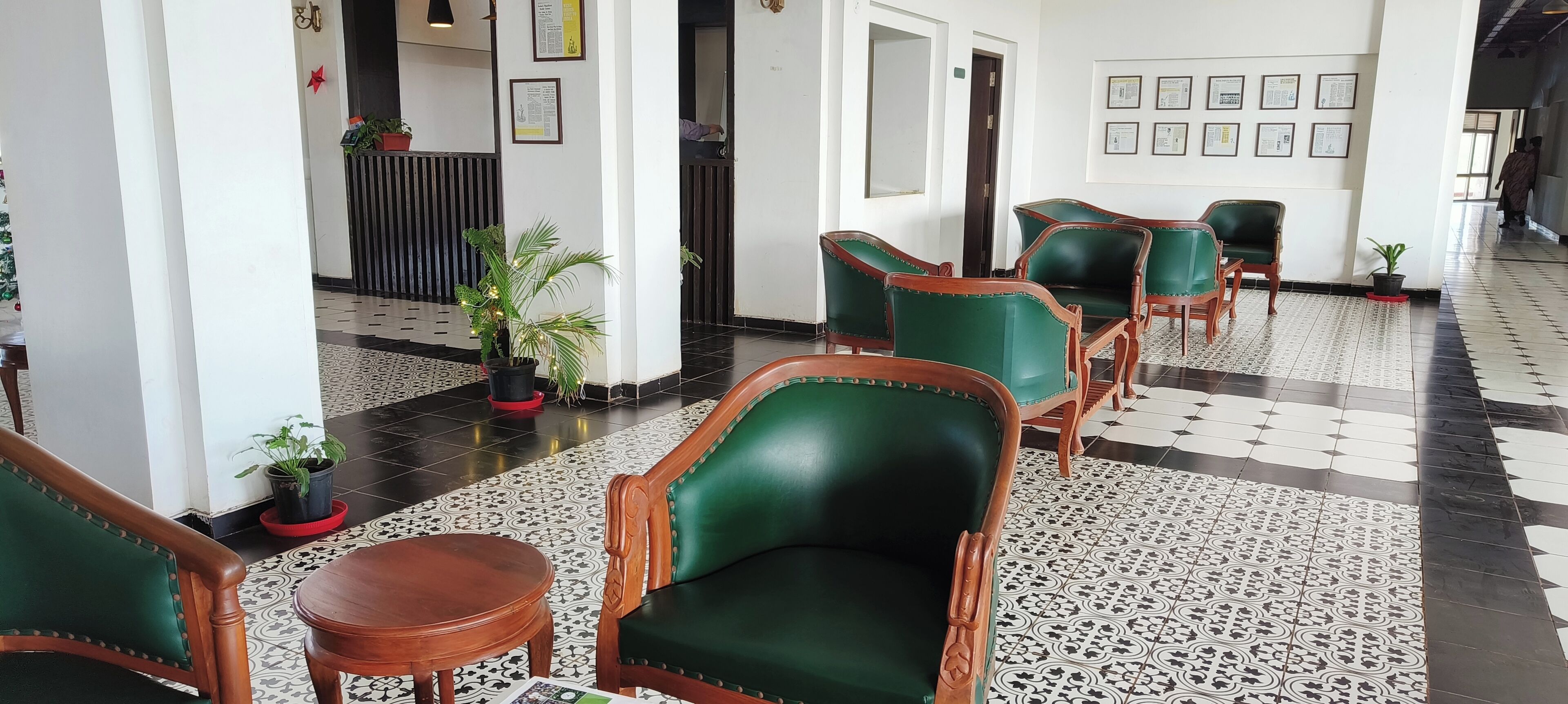 Um hall com poltronas estofadas em verde, um balcão de recepção, plantas em vasos e certificados emoldurados na parede.