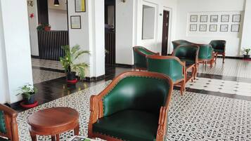 Um hall com poltronas estofadas em verde, um balcão de recepção, plantas em vasos e certificados emoldurados na parede.