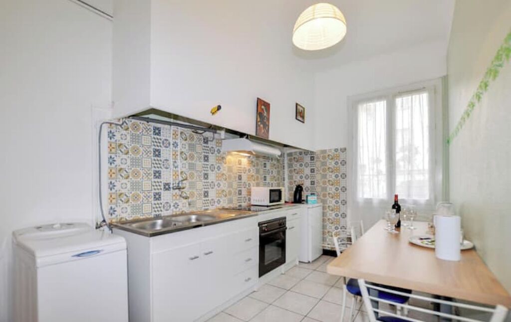 A compact kitchen with white cabinets, a microwave, and a sink. There is a dining table with chairs and a window providing natural light.