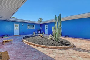 A blue building with a paved patio, a cactus garden, and a wooden bench. - Vibrant Coastal Cottage with Pool (Indian Harbour Beach)