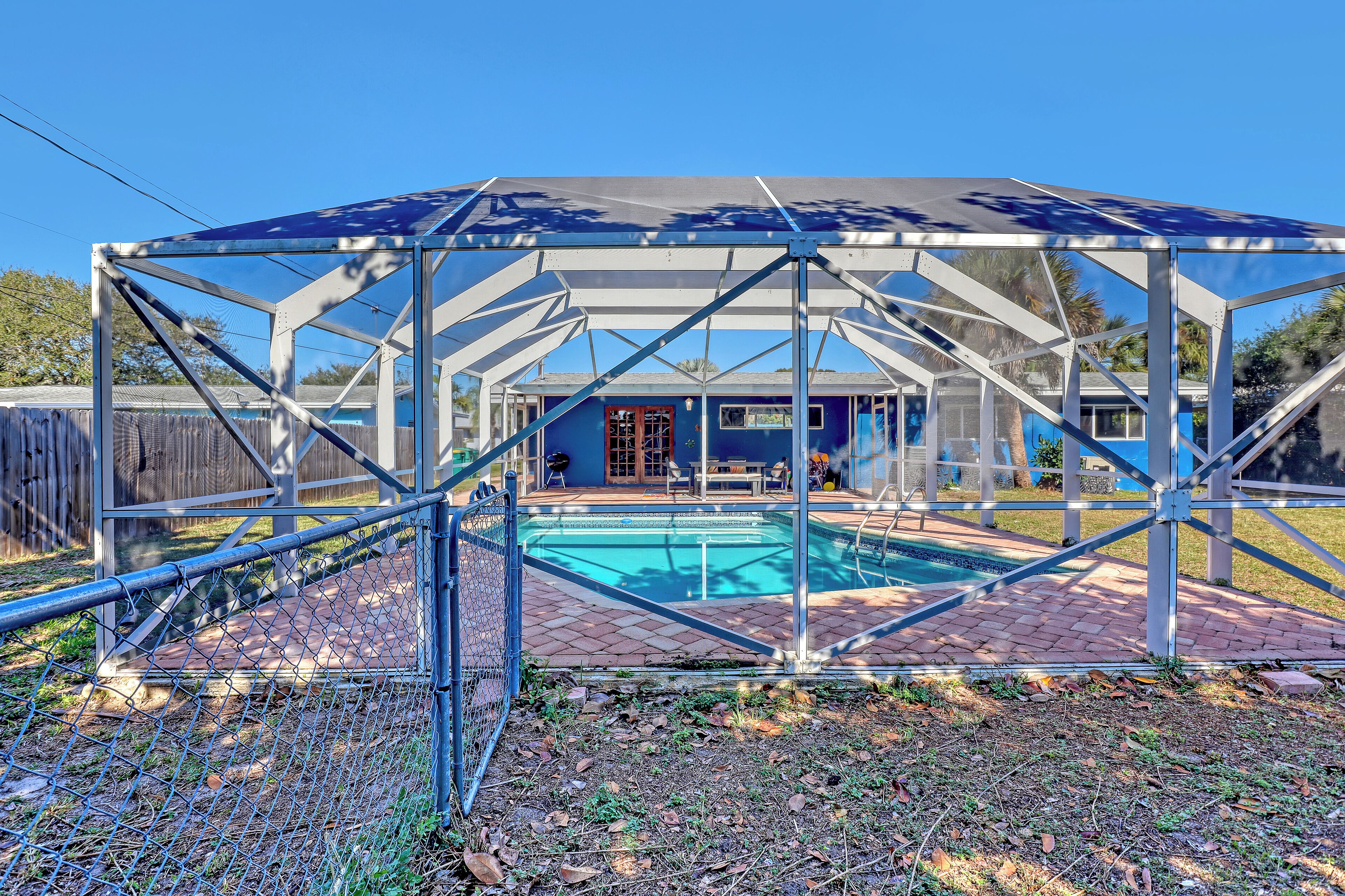 Piscina descoberta coberta com estrutura metálica e toldo azul, rodeada por um pátio de tijolos e uma cerca de arame.