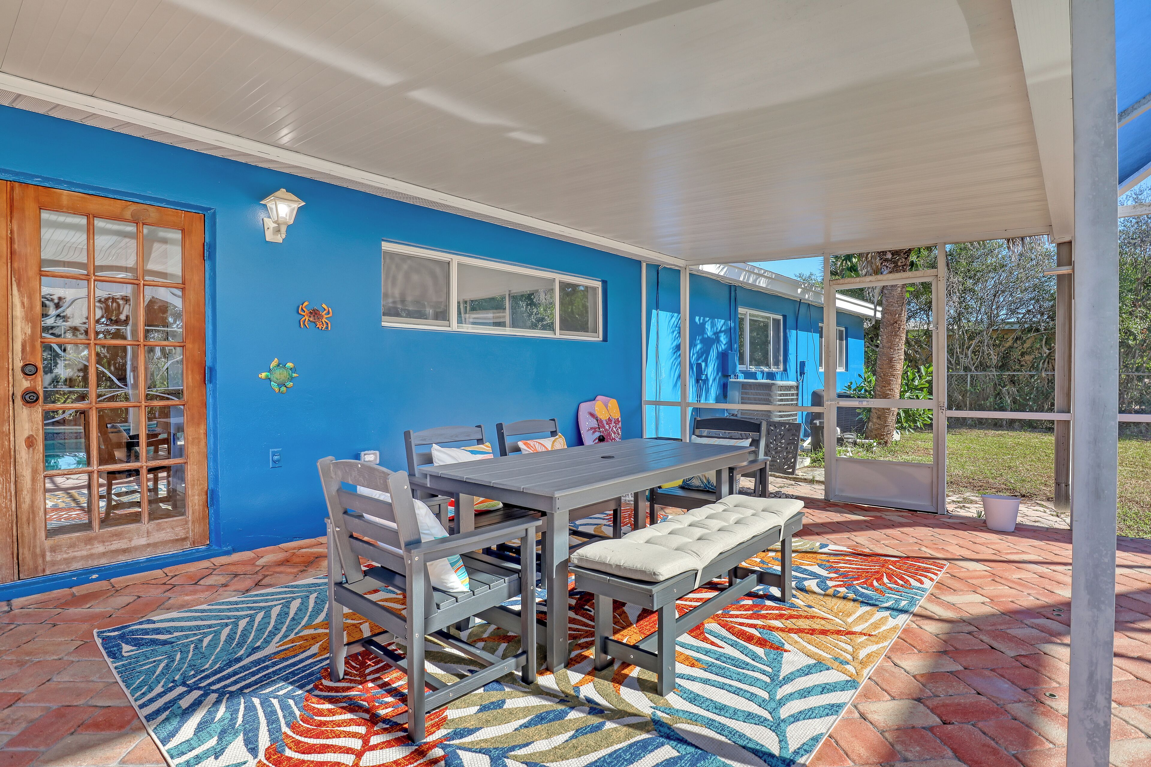 Un patio cubierto con una mesa, sillas, un banco y un tapete estampado.