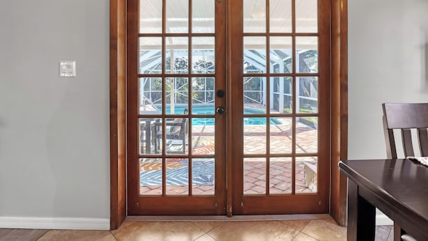 Eine hölzerne Doppeltür mit Glasfeldern, die zu einer Außenpatio mit Pool und überdachtem Bereich führt.