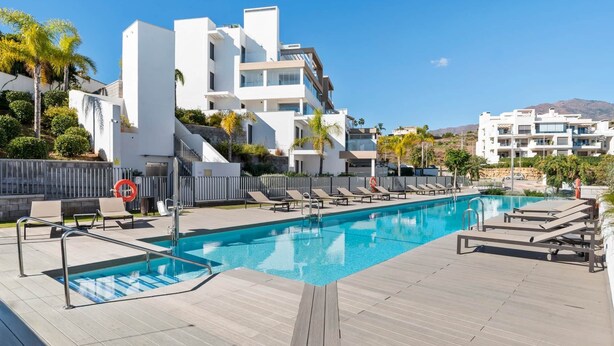 Un hotel moderno con piscina, tumbonas y vistas a las montañas.