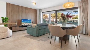 Una sala moderna con televisor de pantalla plana, un sofá, una mesa de comedor con sillas y un amplio ventanal con vistas al exterior.