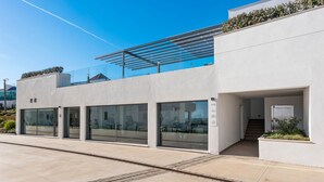 Un edificio moderno con grandes ventanales, un área exterior cubierta y una escalera que conduce a la entrada.