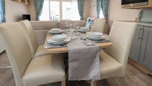 A dining area with a round table set for four, surrounded by cushioned chairs. - Poppy Lodge (Morecambe)