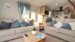 A cozy living room with two sofas, a coffee table, and a small kitchen area in the background. - Poppy Lodge (Morecambe)