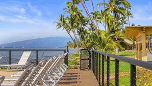 Une terrasse avec des chaises longues donnant sur une étendue d’eau, des palmiers et un paysage montagneux en arrière-plan.