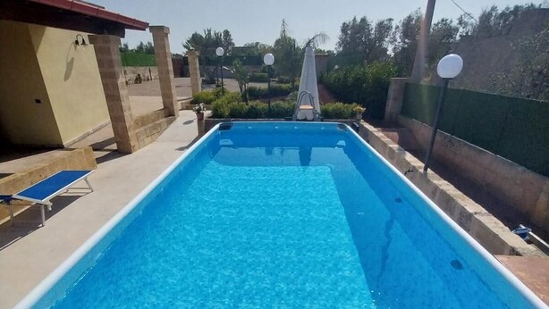 Ein rechteckiger Swimmingpool mit klarem, blauem Wasser, umgeben von einer Betonplattform und einer niedrigen Mauer.