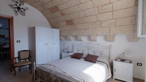 Ein Schlafzimmer mit Ziegeldecke, einem Bett mit Metallgestell, einem weißen Nachttisch und einem Stuhl.