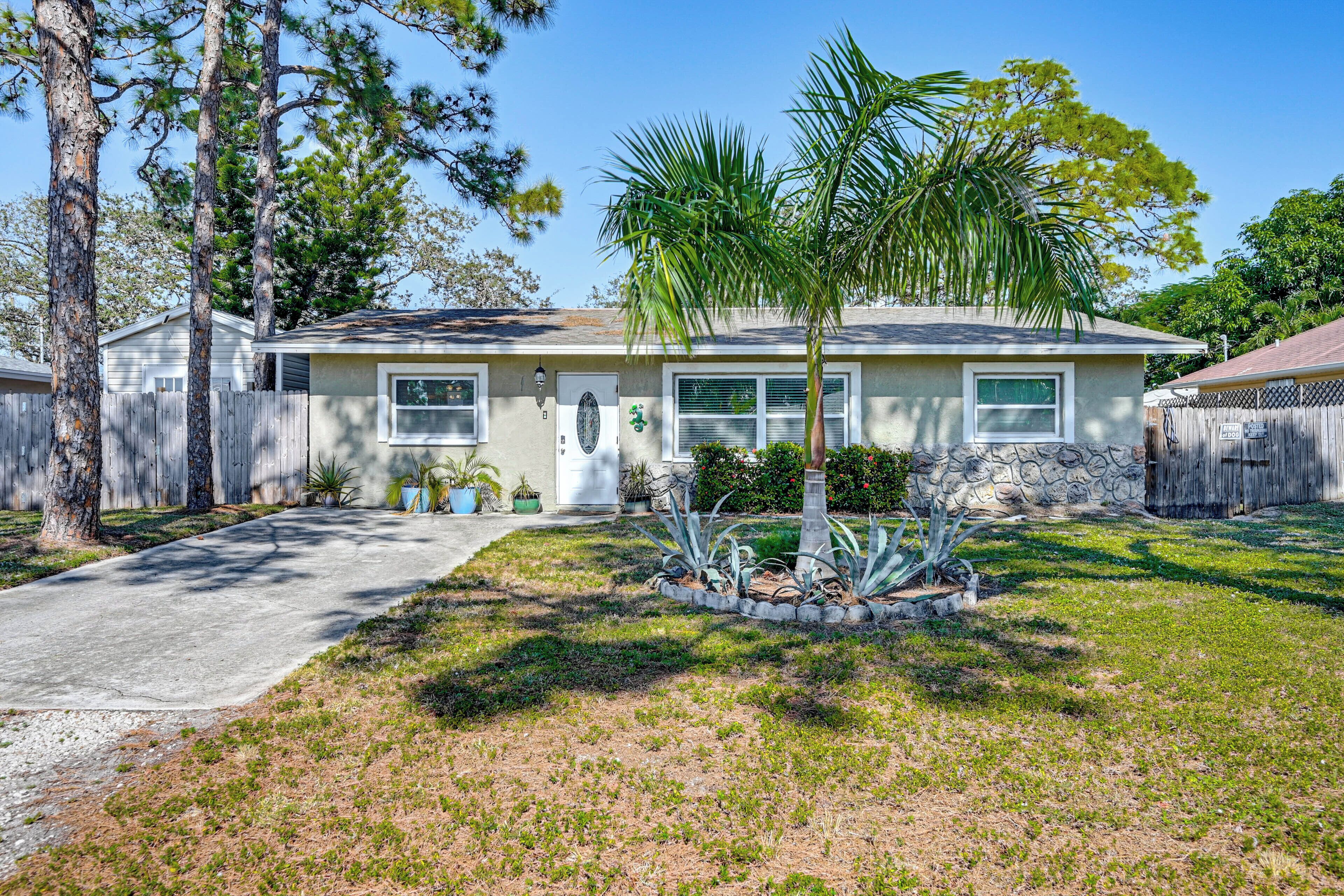 A single-story house with a front yard, a palm tree, and a wooden fence.