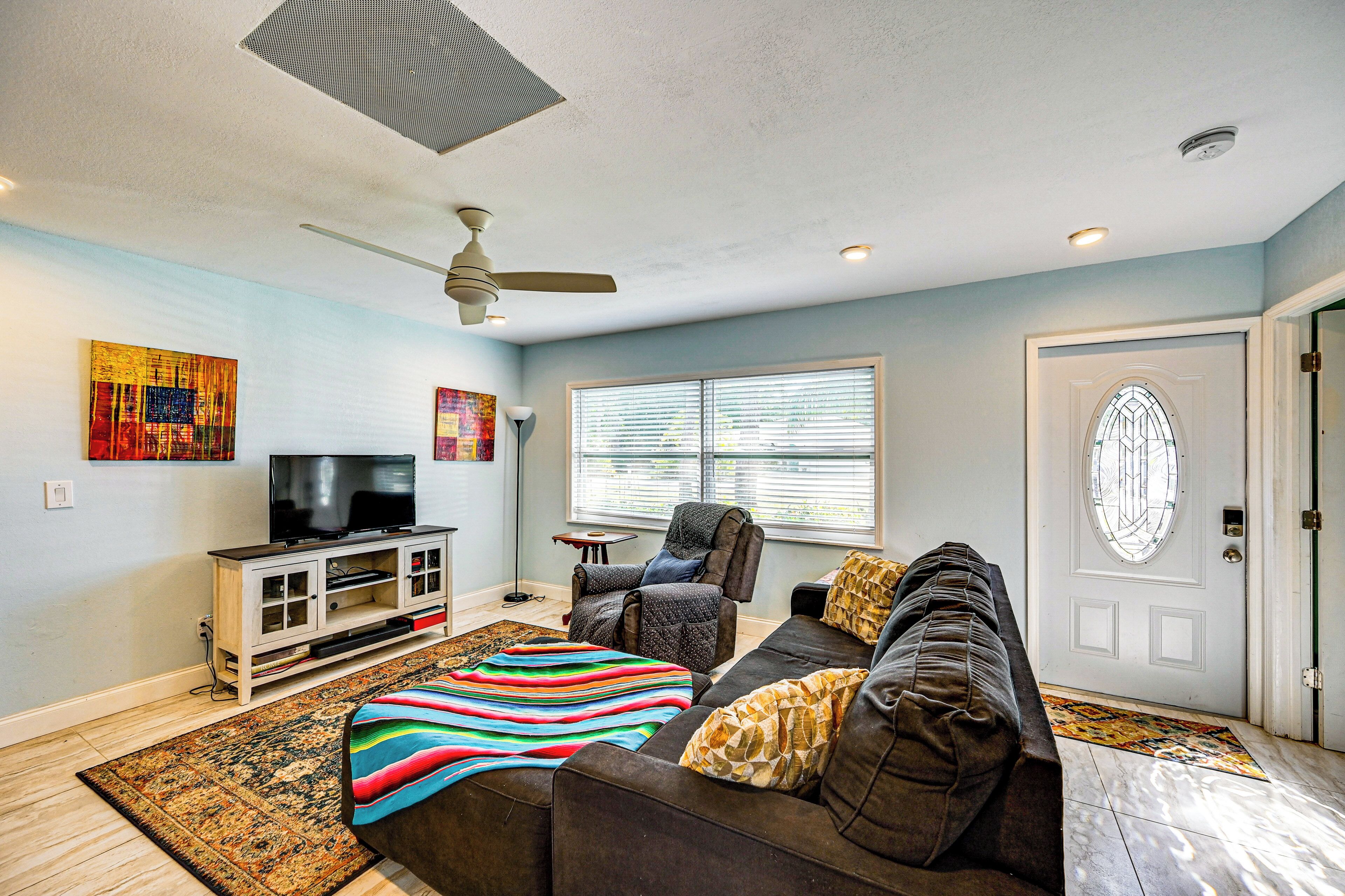 A living room with a sofa, a television on a cabinet, a ceiling fan, and a door with a window.
