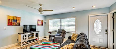 A living room with a sofa, a television on a cabinet, a ceiling fan, and a door with a window.