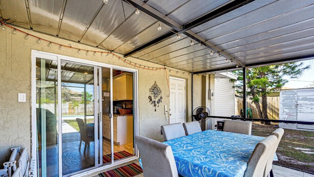 Un patio couvert avec une table et des chaises, une porte-fenêtre coulissante donnant sur un espace intérieur et un ventilateur.