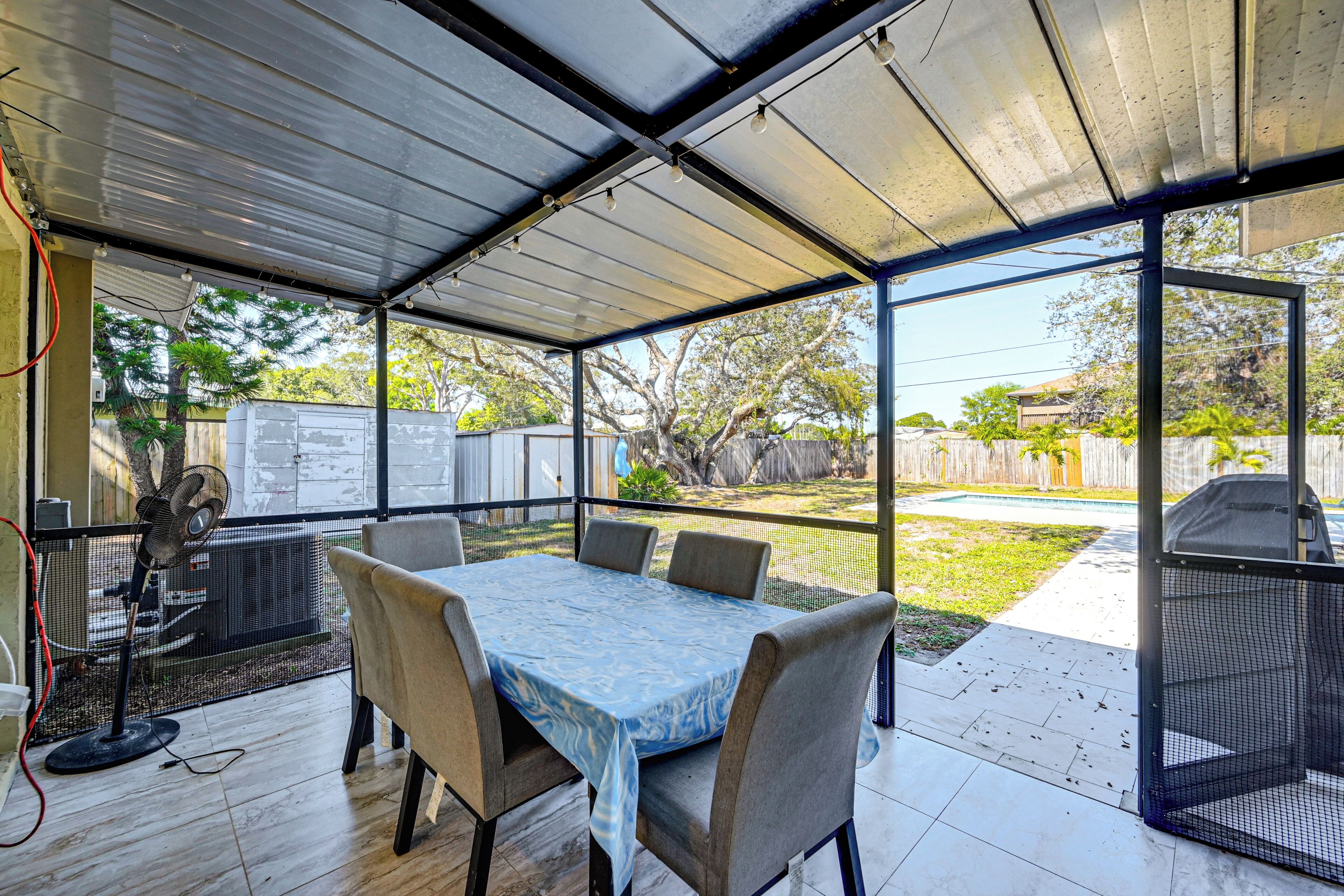 Un porche cubierto con una mesa, sillas, un ventilador y una zona de barbacoa.