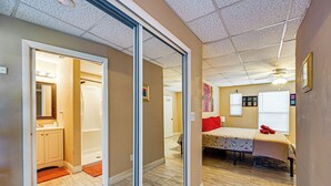Une pièce dotée d’une porte coulissante donnant sur une salle de bain, d’un lit avec un oreiller rouge et d’un ventilateur de plafond.