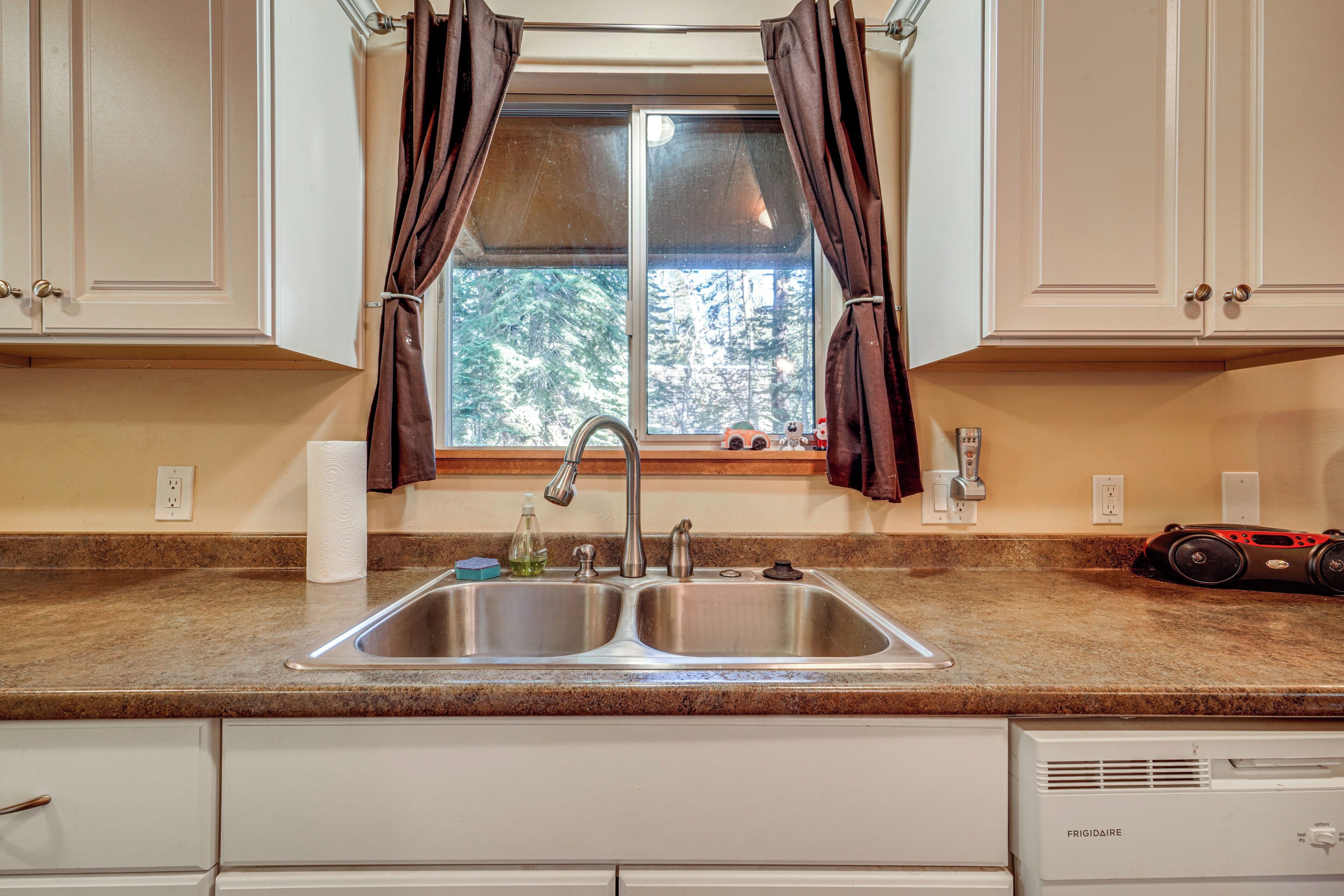 A kitchen with a double stainless steel sink, a window with curtains, and a built-in refrigerator.
