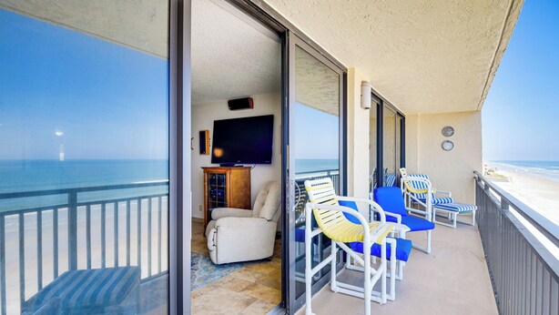 A balcony with a view of the ocean, a television, and several lounge chairs. - Steps to Shore, Pool Access: New Smyrna Beach Gem! (New Smyrna Beach)