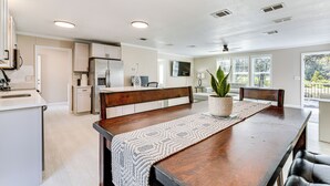 A modern kitchen with white cabinetry, a wooden dining table with a patterned runner, and a potted plant. - 7 Mi to Disney: Pet-friendly Home w/ Yard (Kissimmee)