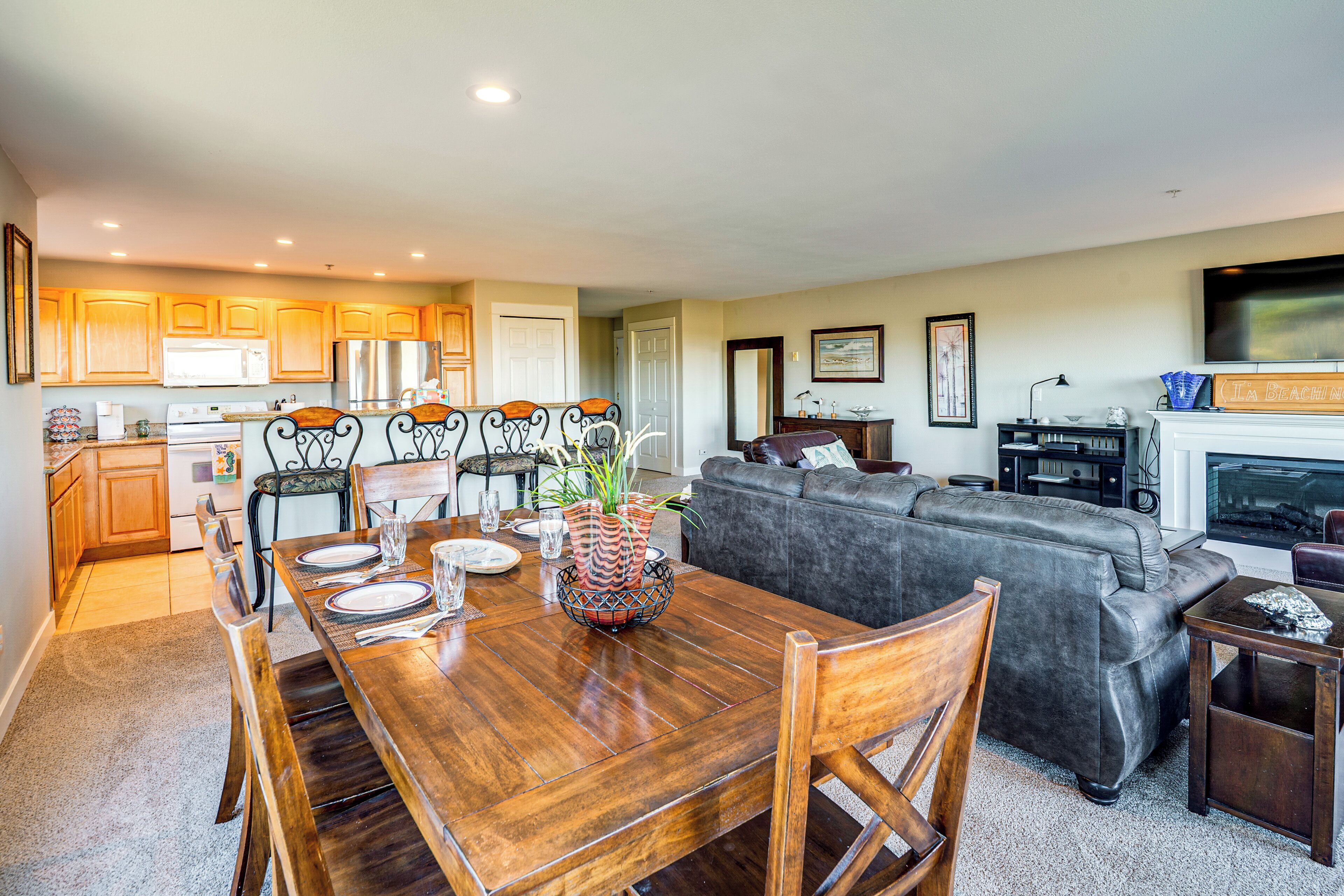 A spacious living area with a dining table set for four, a gray sofa, and a fireplace.