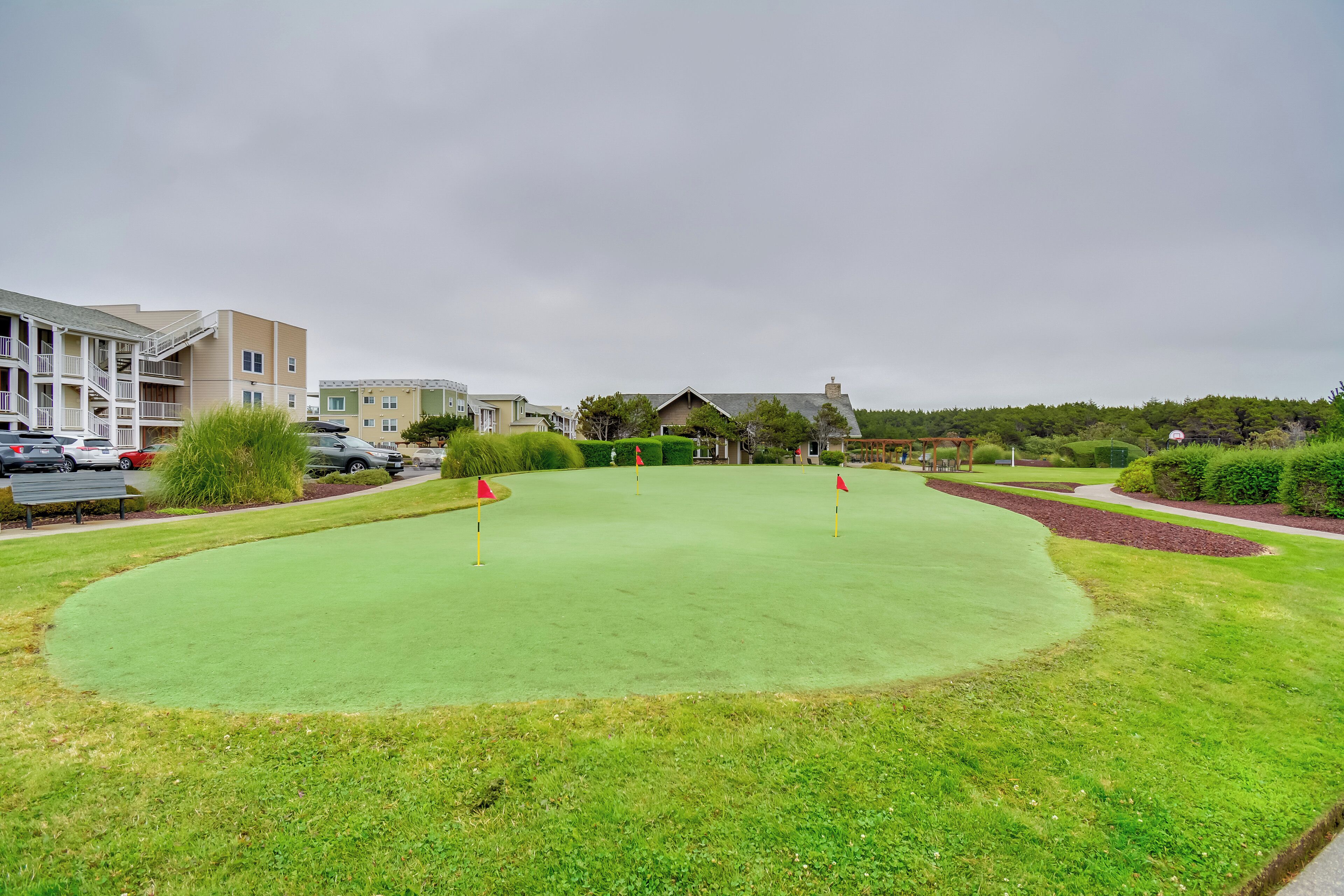 A golf course with a putting green, surrounded by residential buildings and parked cars.