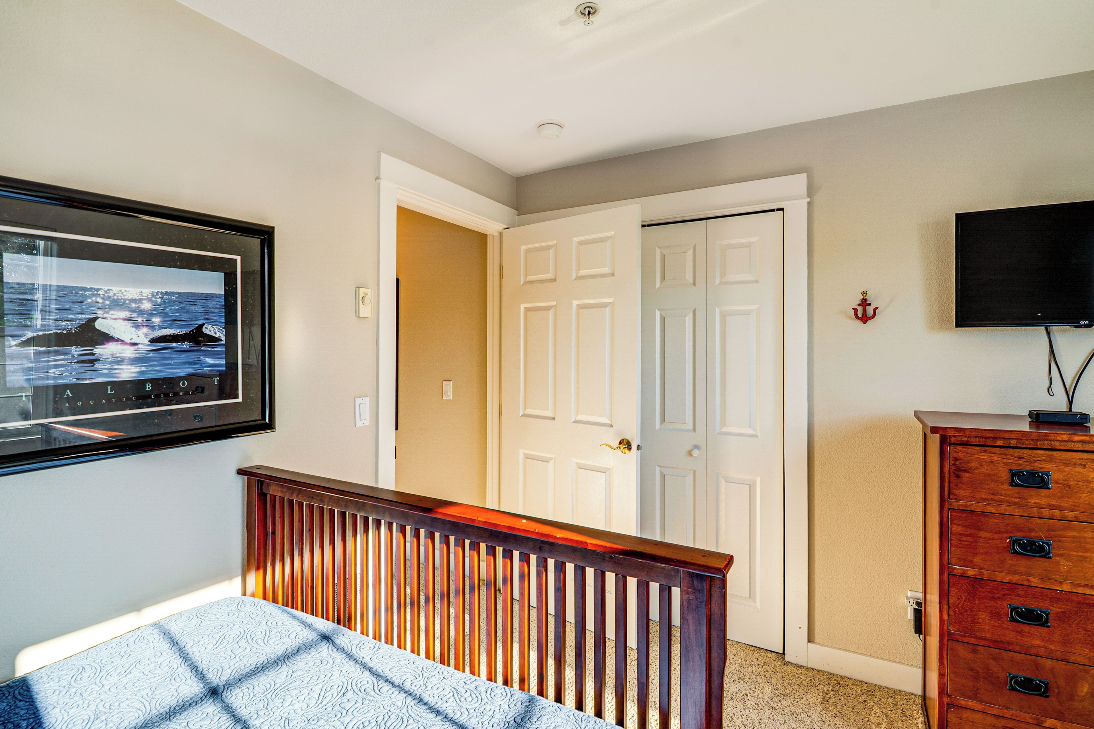 Un dormitorio con cama, cómoda, televisor y puerta que da a otra habitación.