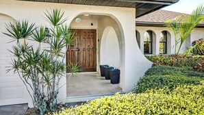 A house with a stucco exterior, a wooden door, and a covered entrance. - New Listing! Canalfront Comfort | Heated Pool, Patio & Palm-Lined Views (Cape Coral)