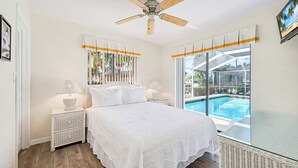A bedroom with a bed, nightstands, a ceiling fan, and a view of a swimming pool. - New Listing! Canalfront Comfort | Heated Pool, Patio & Palm-Lined Views (Cape Coral)