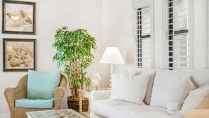 A living room with a wicker chair, a white sofa, a glass coffee table, and a potted plant. - New Listing! Canalfront Comfort | Heated Pool, Patio & Palm-Lined Views (Cape Coral)