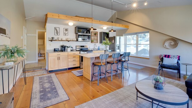 Una cocina moderna con vigas de madera, una isla central con taburetes de bar y un comedor con una mesa redonda.