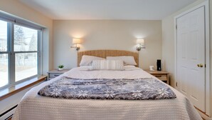 Un dormitorio con una cama grande, dos lámparas de noche, una mesita de noche, una ventana y una puerta.